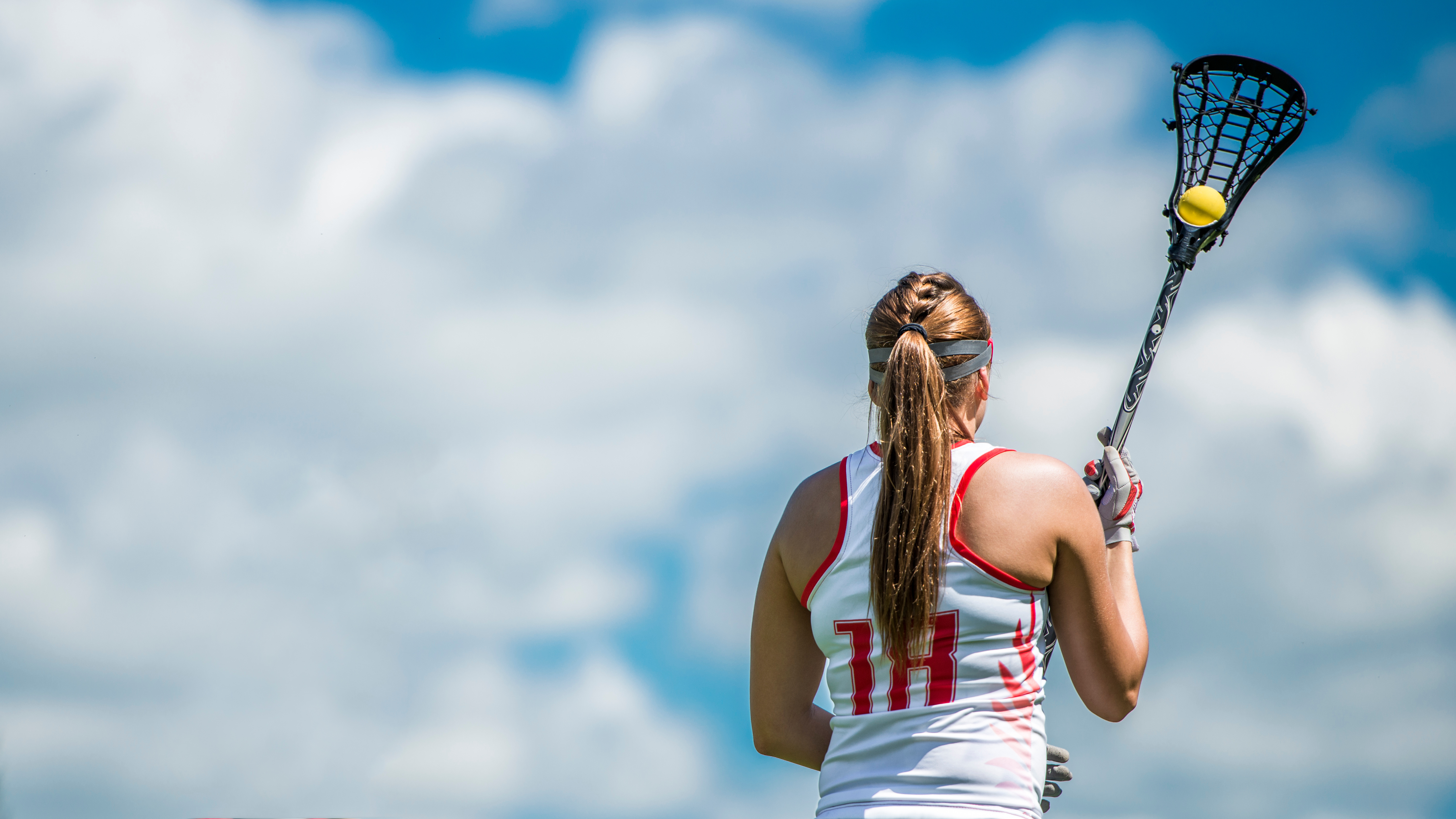 Girl holding lacrosse stick with a lacrosse ball wearing lacrosse gloves.
